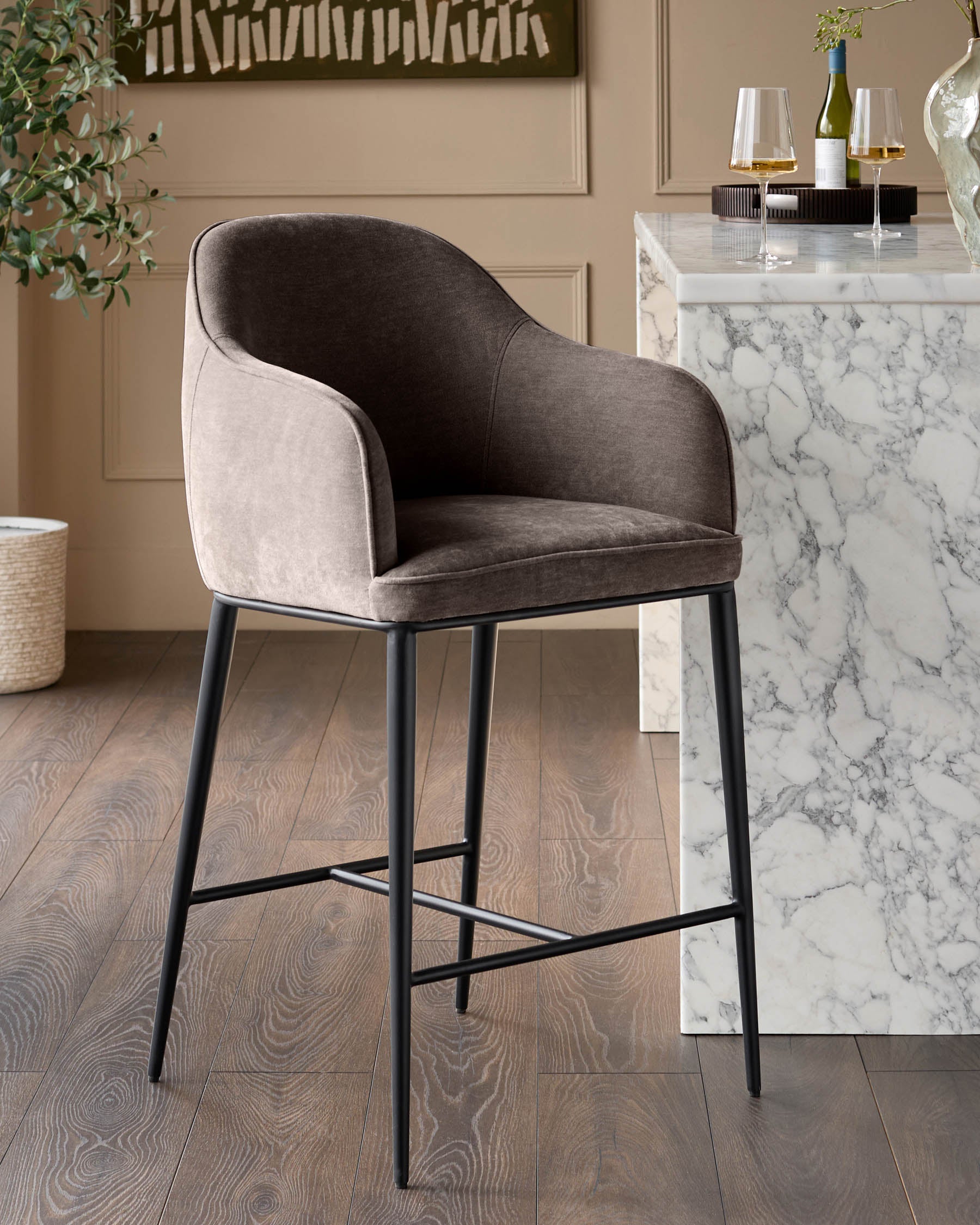 Mocha fabric bar stool with curved back and black metal legs, positioned at a marble counter in a modern dining setting.