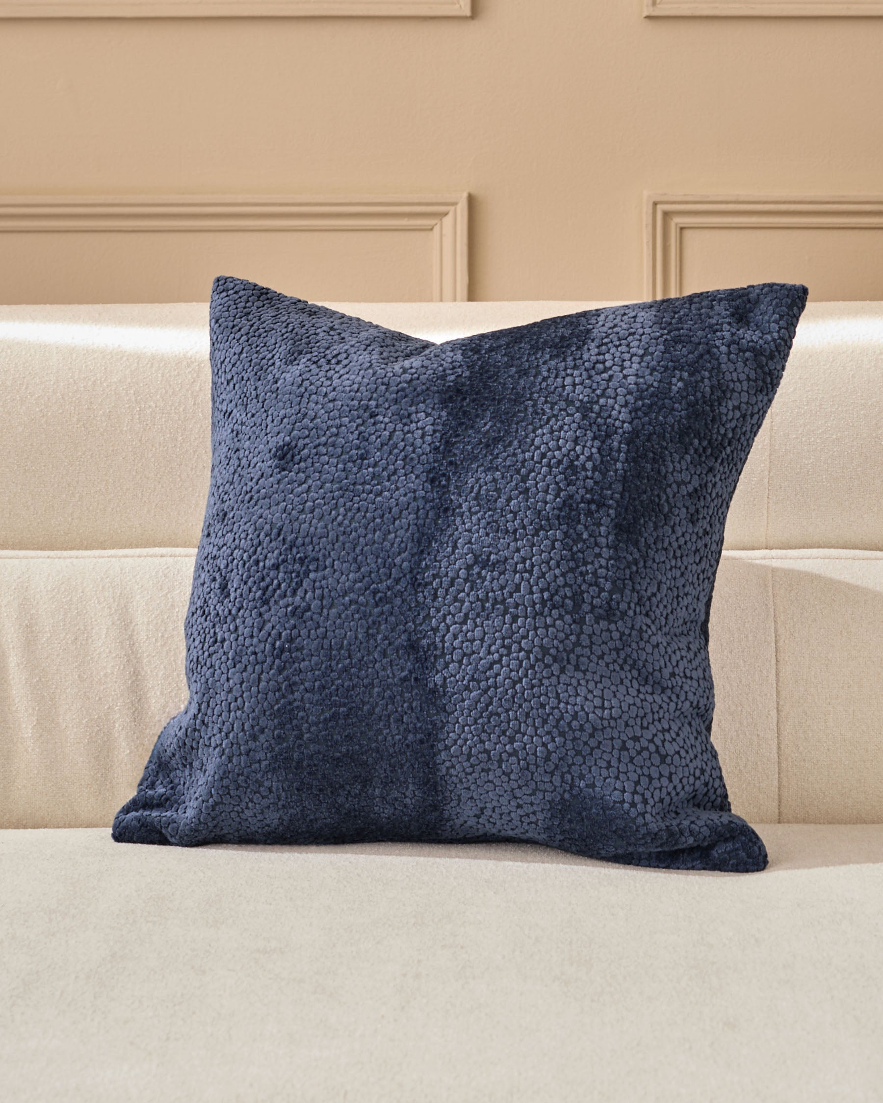 Navy textured cushion with a boucle weave, displayed on a cream upholstered sofa against a neutral wall.