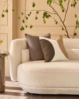 Harmony medium cushion in natural color displayed on a cream armchair with decorative pillows in a bright, minimalist interior.