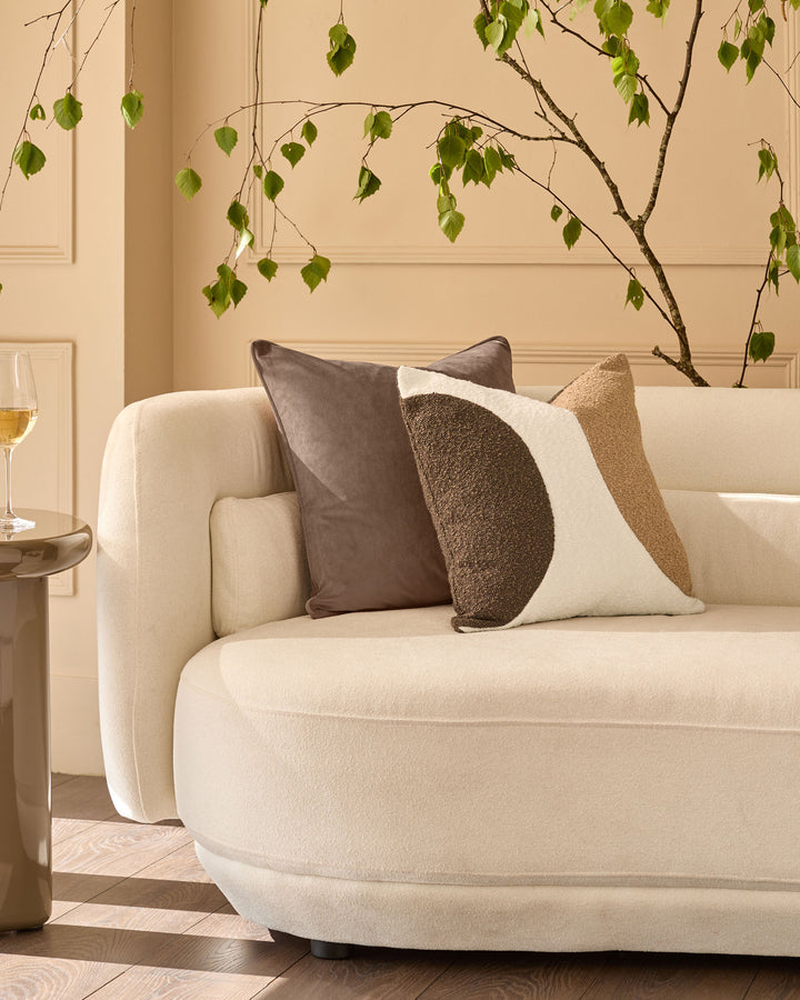 Harmony medium cushion in natural color displayed on a cream armchair with decorative pillows in a bright, minimalist interior.