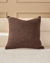 Brown textured cushion with piping on a cream upholstered sofa against a beige paneled wall.