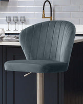 Harper velvet gas lift bar stool in blue-grey with vertical channel stitching and brushed metal base, shown at kitchen island.