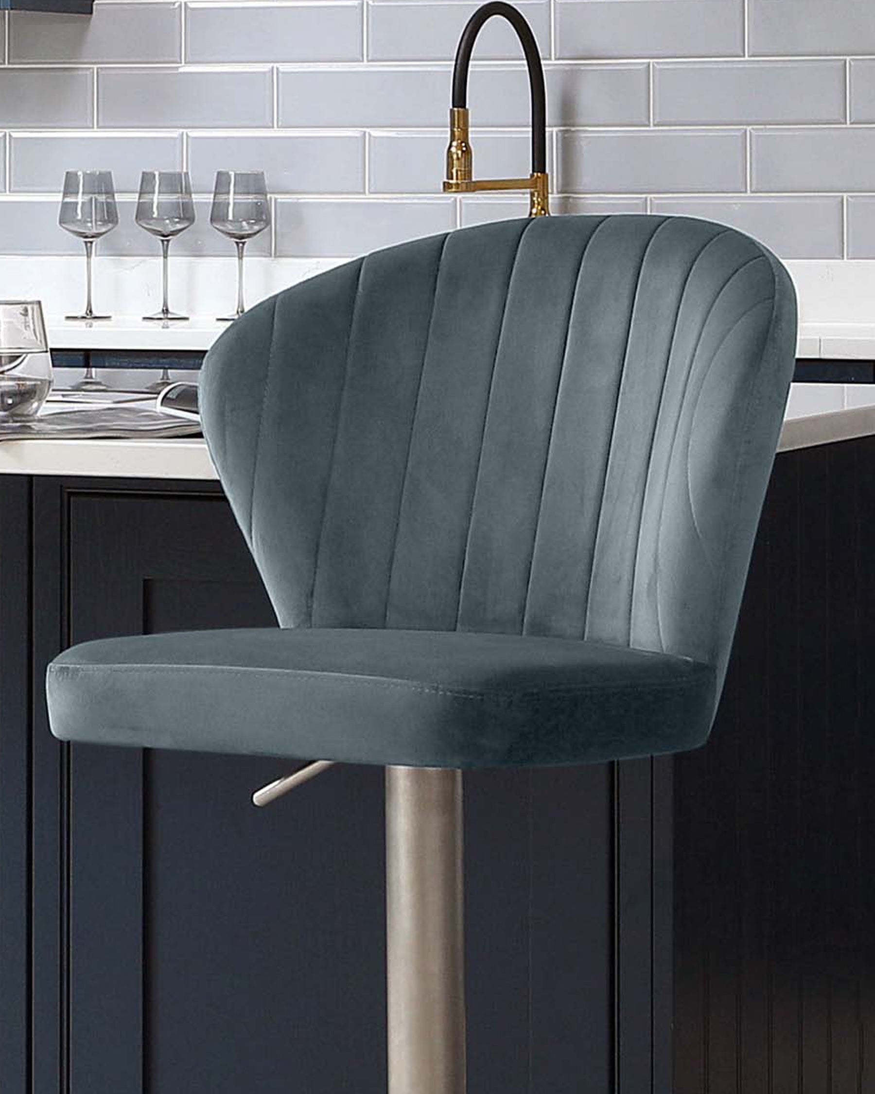 Harper velvet gas lift bar stool in blue-grey with vertical channel stitching and brushed metal base, shown at kitchen island.