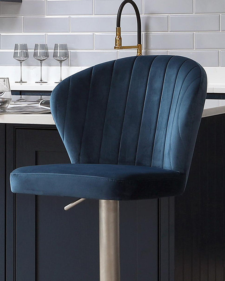 Harper velvet gas lift bar stool in dark blue with vertical channel tufting, brushed metal base, positioned at kitchen island.