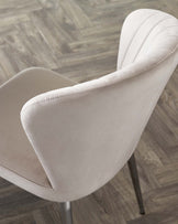 Harper dining chair in champagne velvet, side view showing curved backrest and black metal legs on wood flooring.