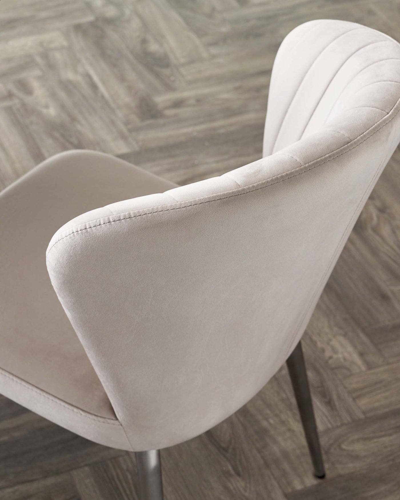 Elegant modern dining chair with a curved backrest and vertical stitching detail, upholstered in a light grey fabric, standing on slender metal legs with a matte finish.