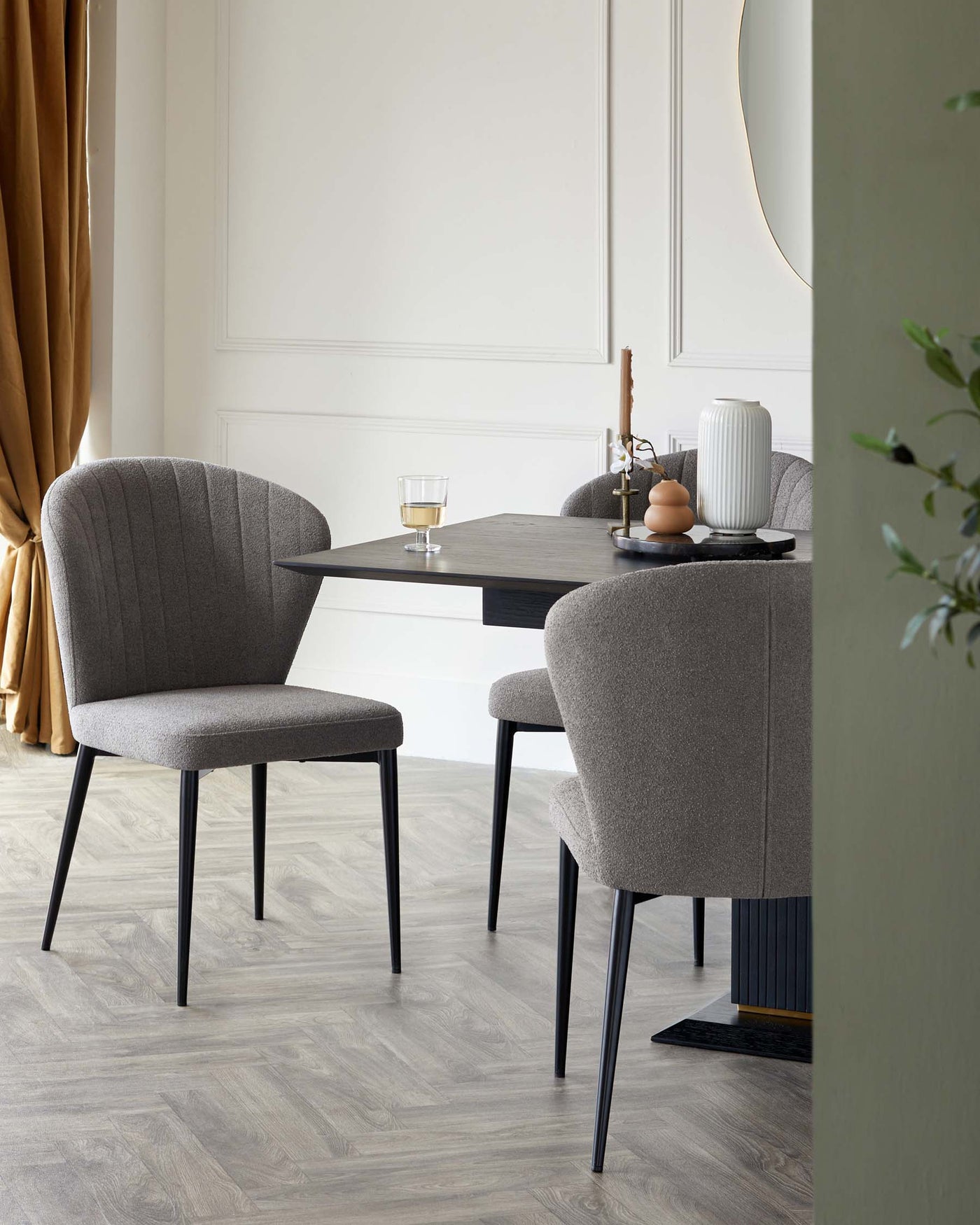 Modern minimalist dining set featuring a sleek rectangular table with a dark wood finish and black metal legs. Accompanied by two upholstered dining chairs in a textured grey fabric with vertical stitching on the backrest and elegant black metal legs. The set is staged in a contemporary room with neutral walls and light wood flooring.