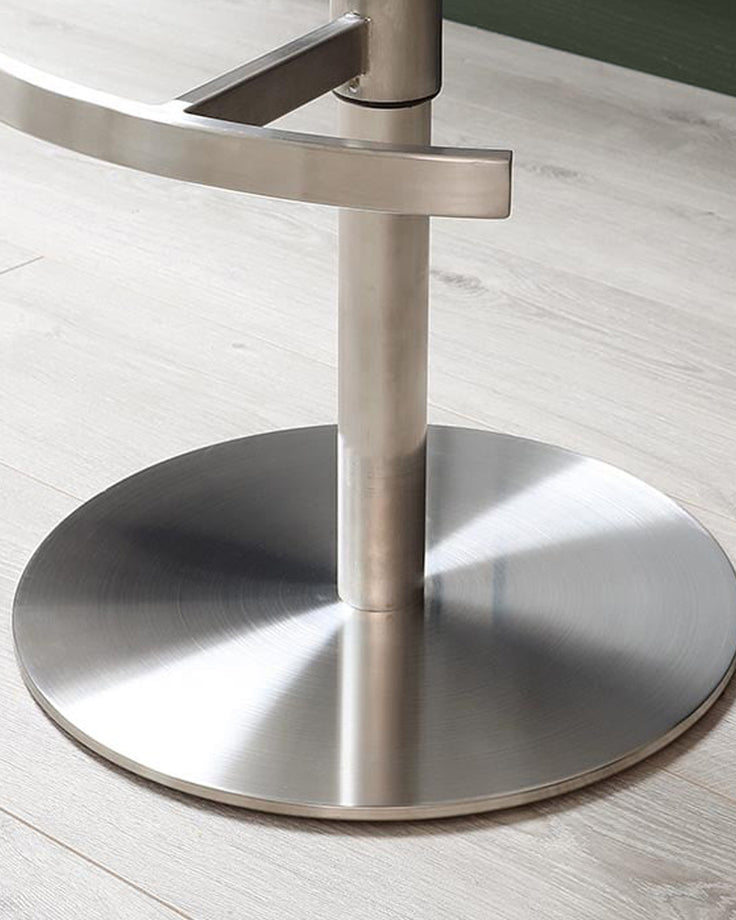 Brushed stainless steel pedestal base with circular footplate and vertical support pole, viewed from above on light wood flooring.