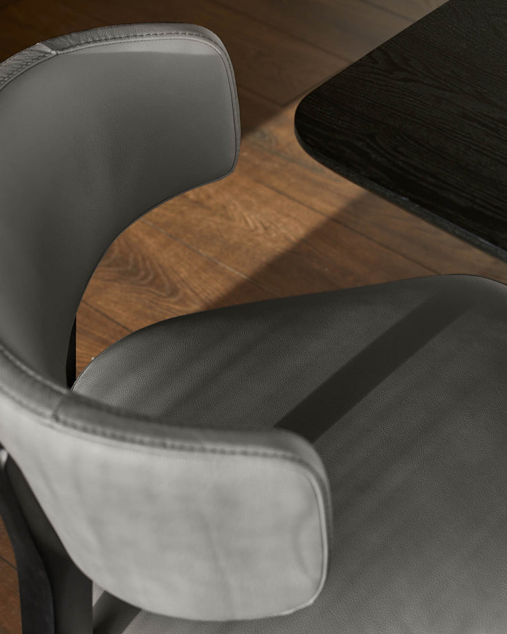 Close-up of a modern grey leather chair next to a dark wooden table on a wood floor.