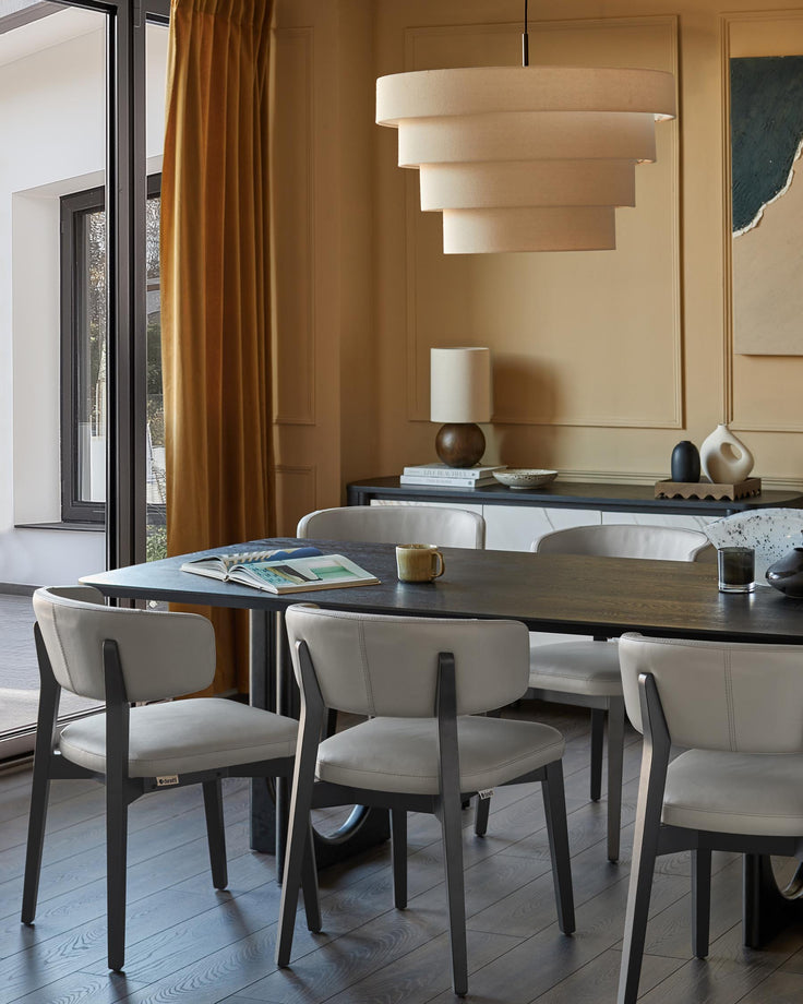 Dining room with dark wood table, grey leather chairs, and a beige tiered light fixture. A sideboard sits against the wall.