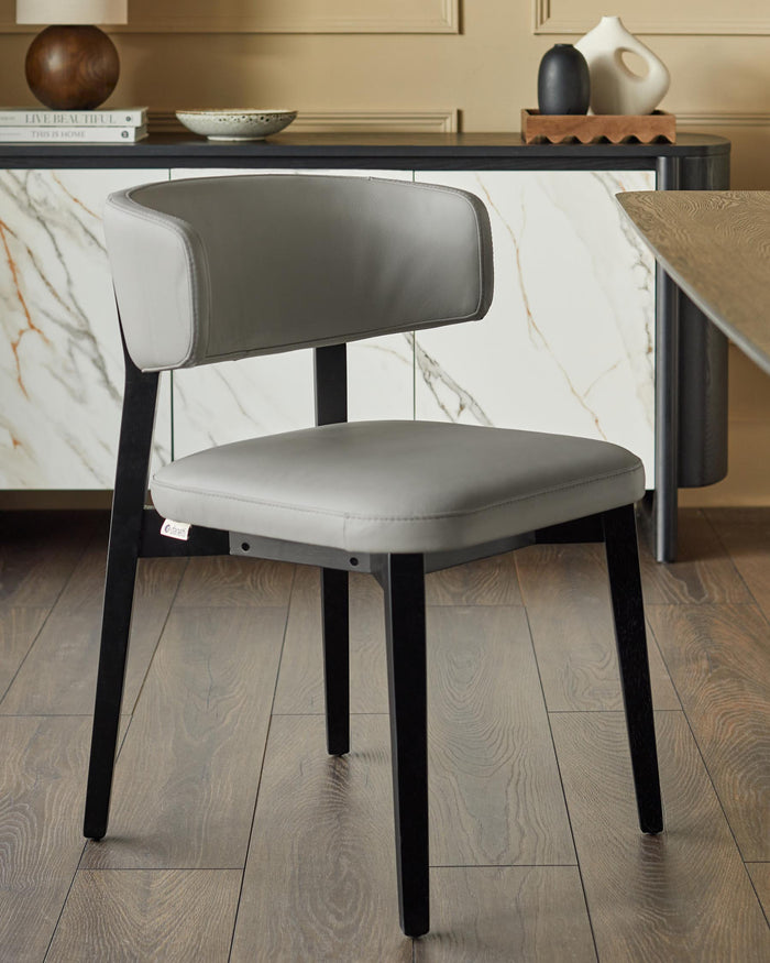 A grey leather dining chair with a sleek black frame, sat on a dark wooden floor in a stylish dining room.
