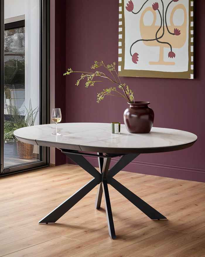 Round dining table with a marble top and black, cross-legged base. Vase and wine glass on table.