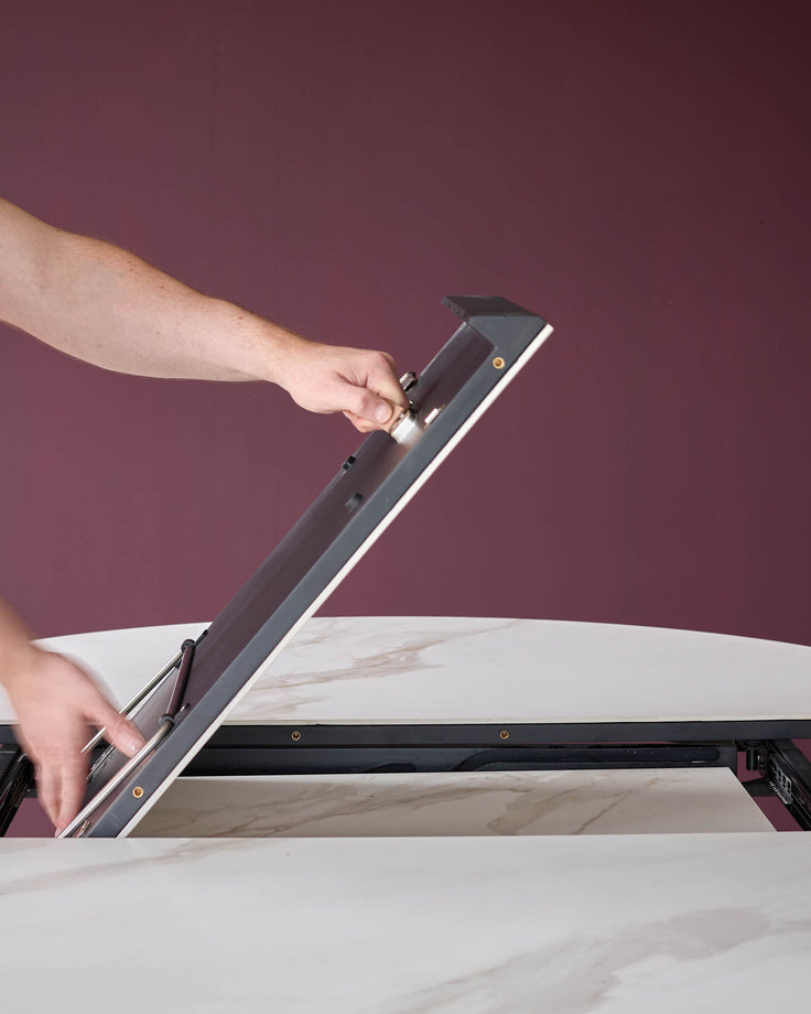 An extendable dining table with a faux marble finish, being assembled by hand.