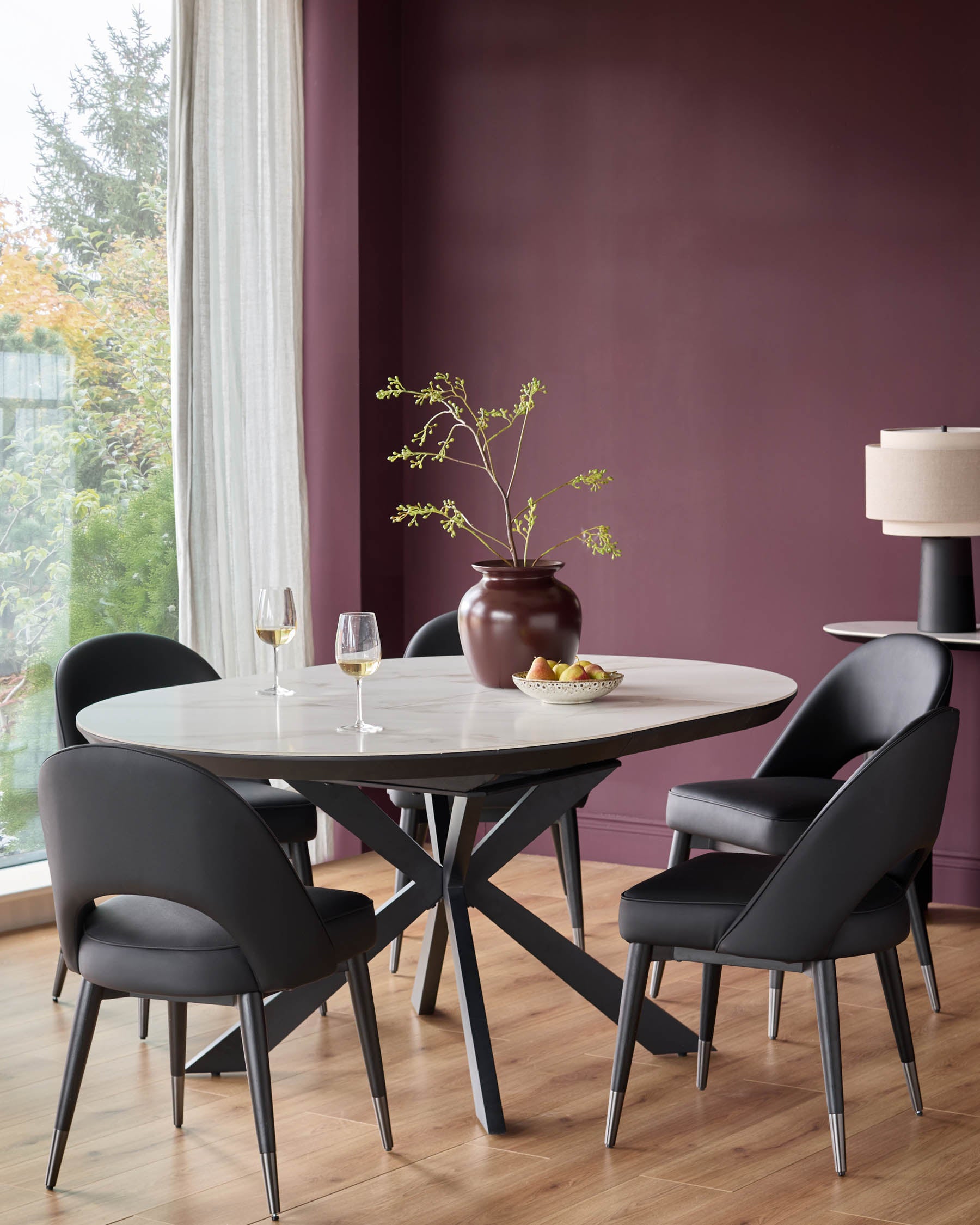 A modern dining set with an oval marble table and four sleek black chairs, complemented by a minimalist vase and fruit bowl.