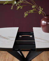 A modern, extendable dining table with a faux marble top and striking black base. A floral centrepiece adds a touch of elegance.