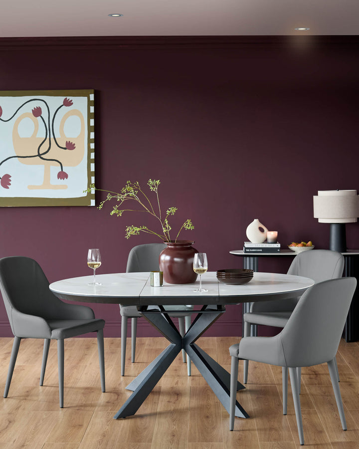 A modern dining set featuring a round marble table with grey chairs, set against a deep burgundy wall.