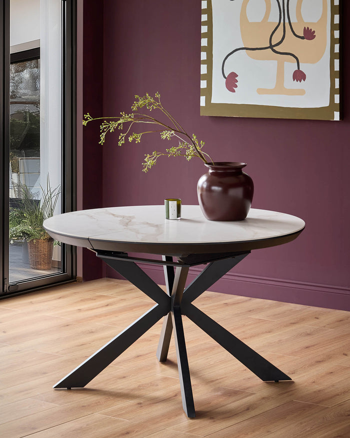 A round marble-topped dining table with a dark, geometric base stands in a room with a contemporary aesthetic.
