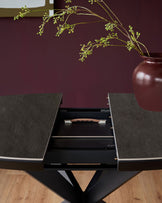 Hayden round extending dining table with dark grey ceramic top and black base, showing open drawer with wooden handle detail.