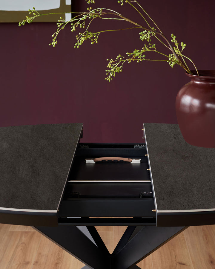 Hayden round extending dining table with dark grey ceramic top and black base, showing open drawer with wooden handle detail.