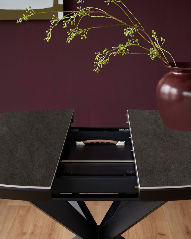Hayden round extending dining table with dark grey ceramic top and black base, showing open drawer with wooden handle detail.