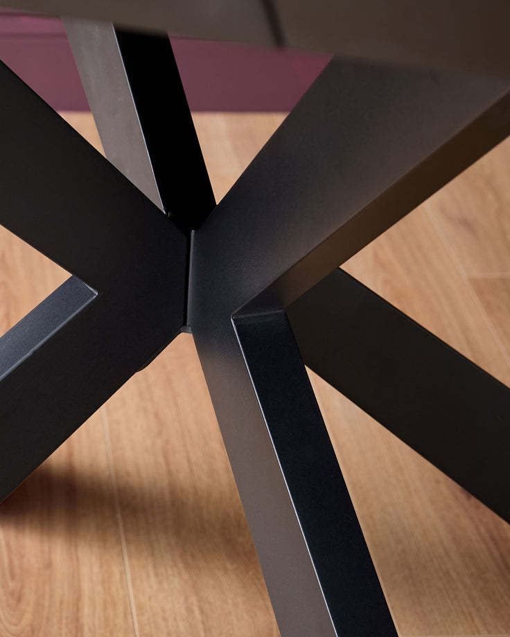 Dark grey metal base with geometric X-frame design viewed from above on wooden floor.