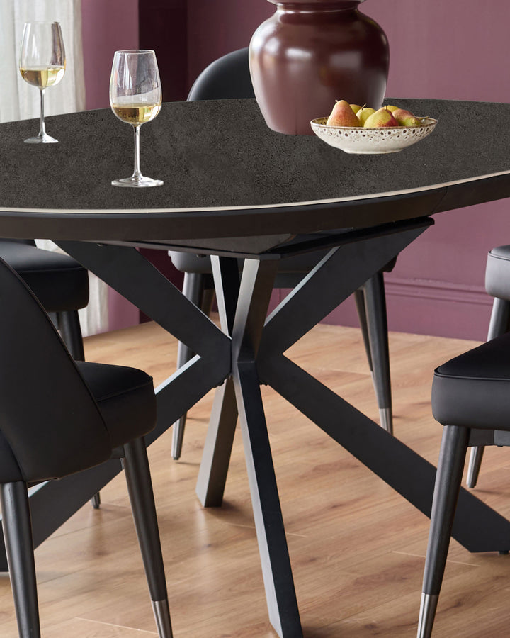 Hayden round extending dining table in dark grey ceramic with black base and metal feet, styled with chairs and tabletop decor.