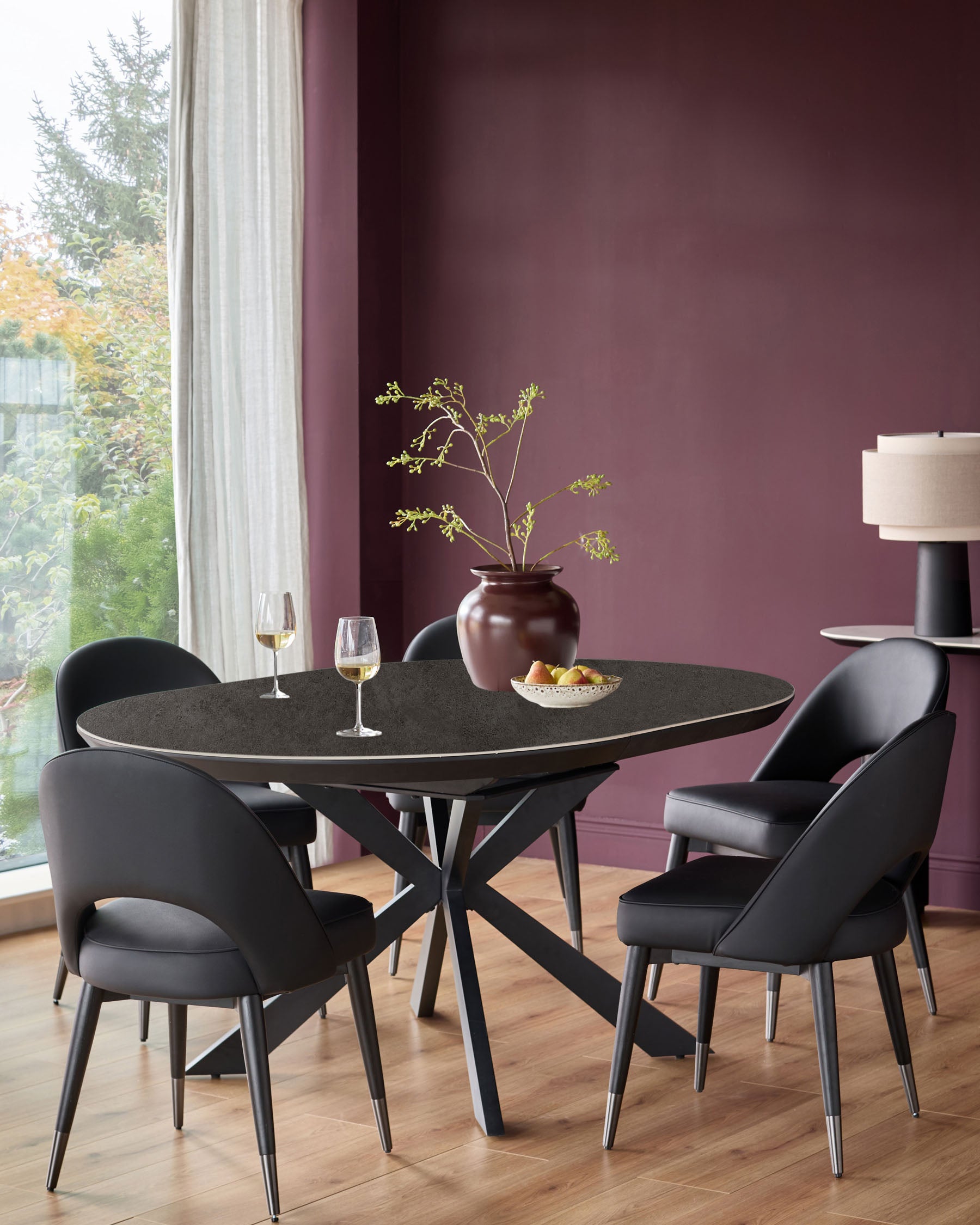 Hayden round extending dining table in dark grey ceramic with black pedestal base, seated with black chairs in modern dining room.