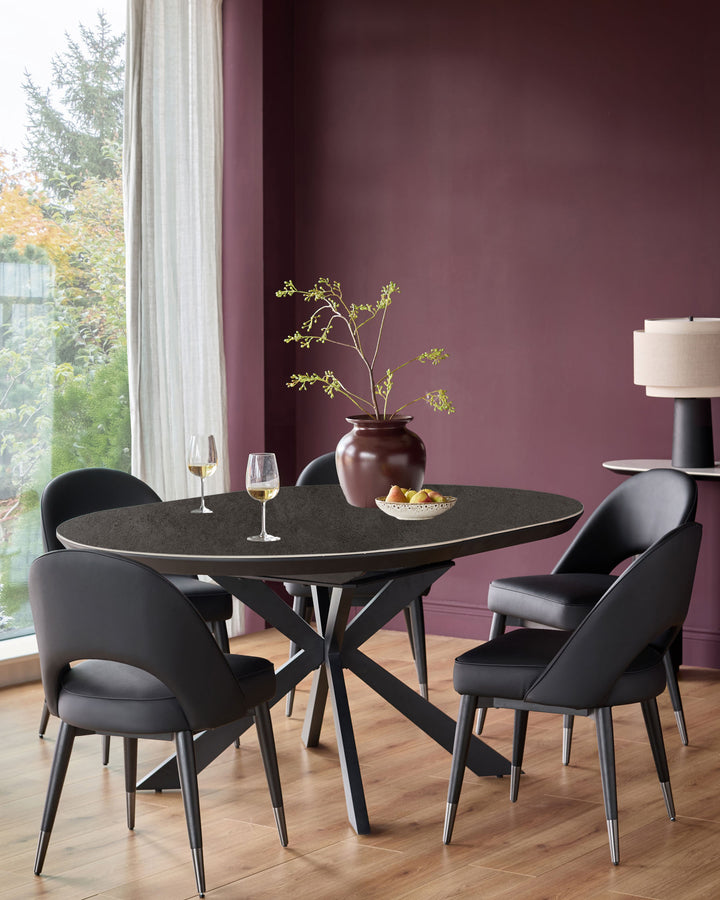 Hayden round extending dining table in dark grey ceramic with black pedestal base, seated with black chairs in modern dining room.