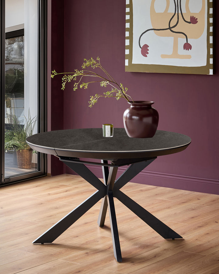 Hayden round extending dining table with dark grey ceramic top and black X-frame base in modern interior setting.