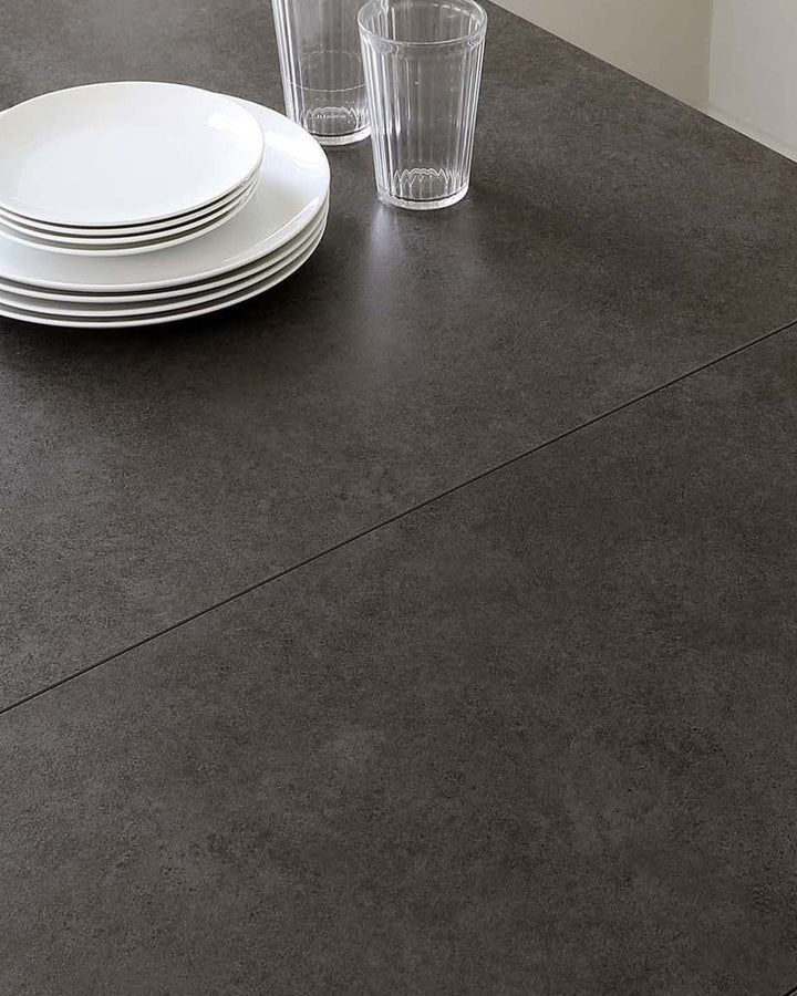 A sleek dark countertop displays stacked white plates and clear glasses, creating a modern dining setting.