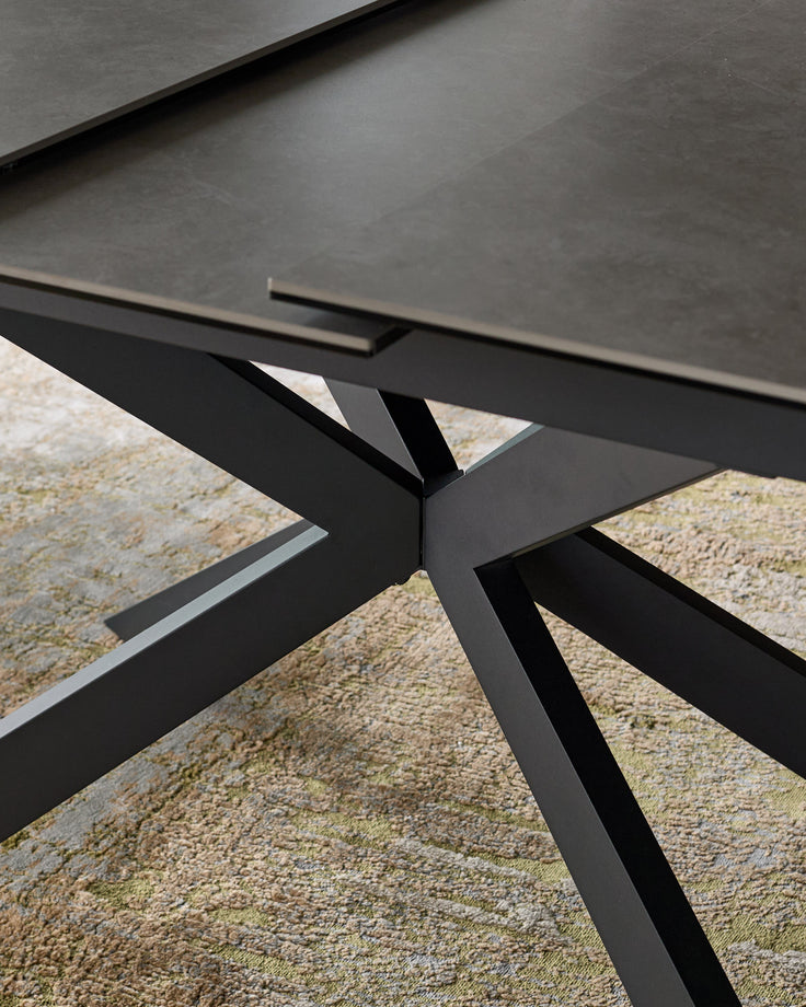 Black metal X-frame base detail of Hayden extending dining table with grey ceramic top, close-up side view.