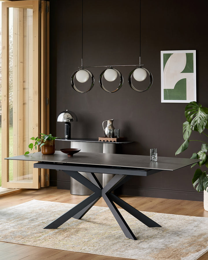 Hayden extending dining table in light grey ceramic with black metal X-frame base, shown in modern room setting.