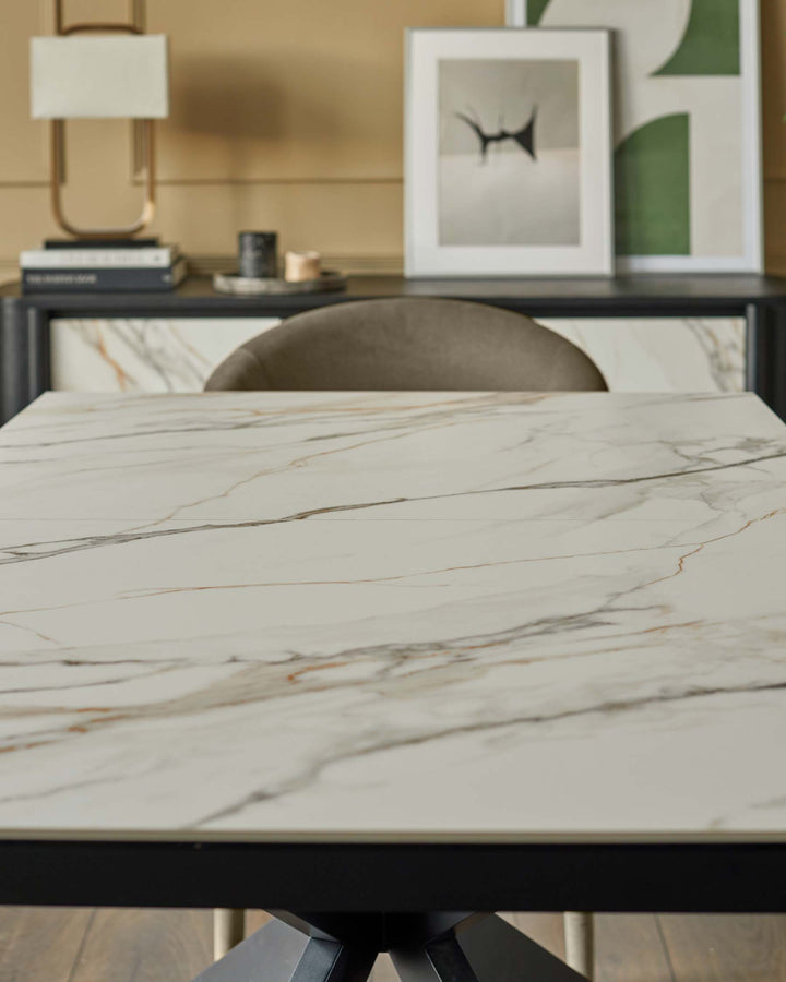 A modern dining table with a marble-effect top sits in front of a sideboard with artwork and a lamp.