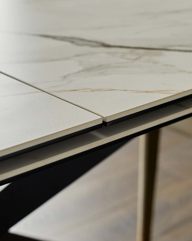 Close-up of a modern extendable dining table with a white marble-effect top and black and metal legs.