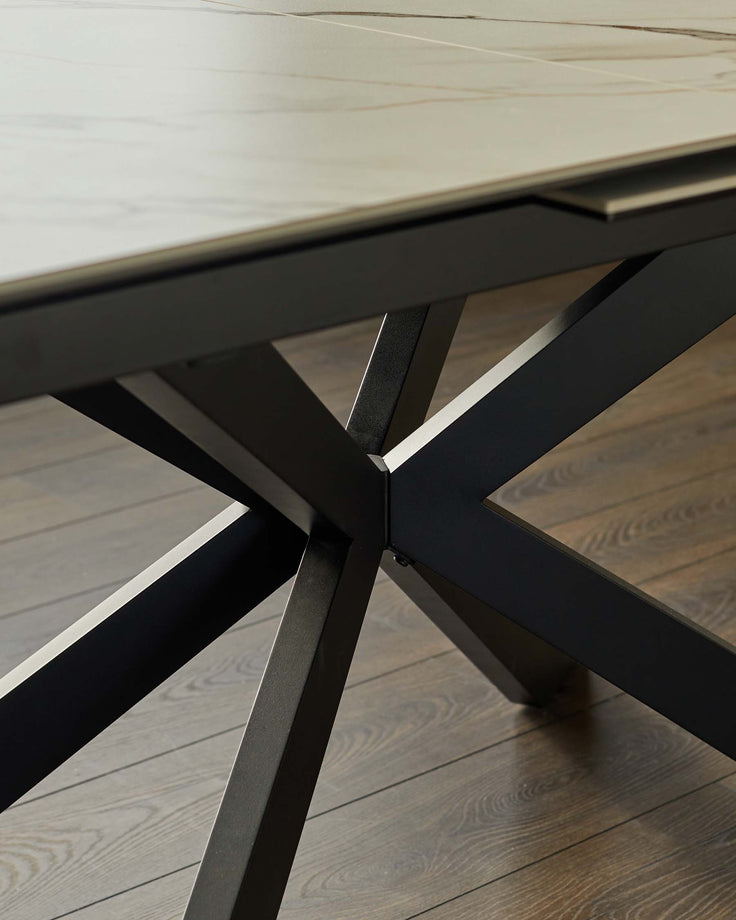 Close-up of a modern dining table with a dark metal cross-legged base and light-coloured top.