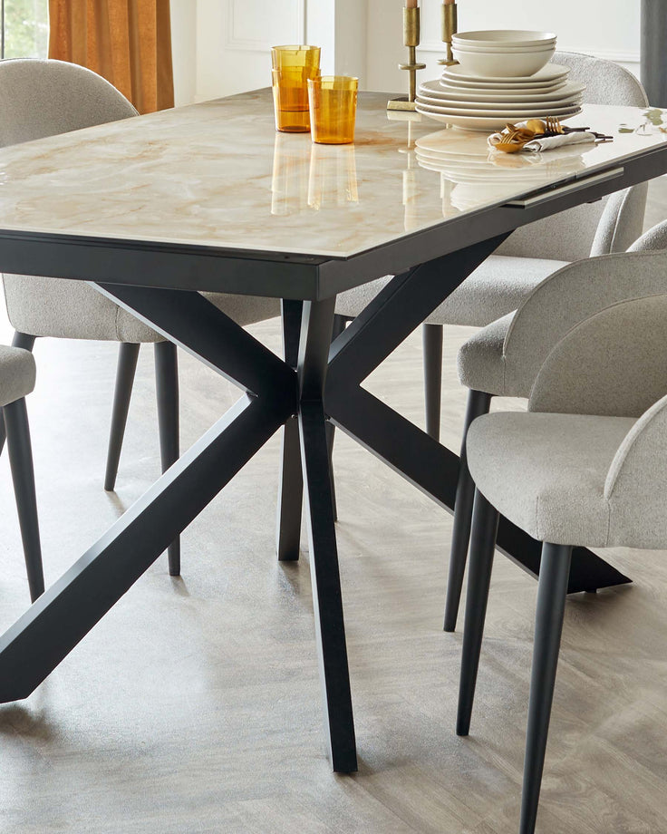 Modern dining set featuring a rectangular table with a marble tabletop and a matte black geometric metal base. Accompanying the table are grey upholstered chairs with a curved backrest and slender black legs. The setting is elegant and contemporary.