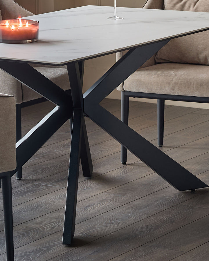 Hayden 6-seater dining table with white ceramic top and black X-frame metal base, styled with candle and place setting.