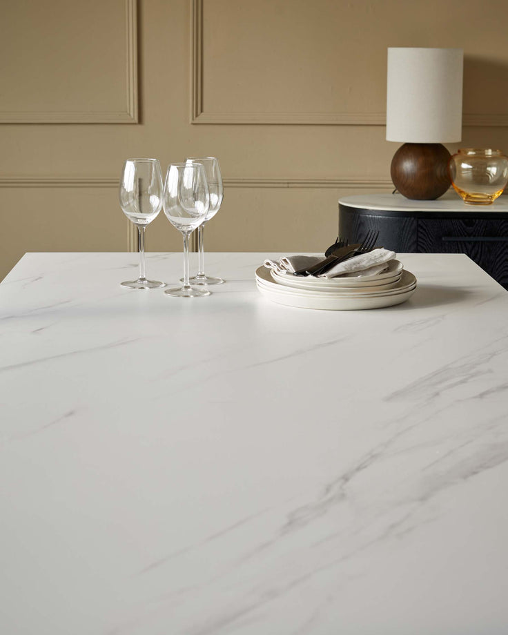 Hayden white marble dining table with place settings, wine glasses, and tableware displayed on top.
