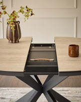 Hayden round extending dining table with natural travertine top and black X-frame base, shown with leaf extension open.