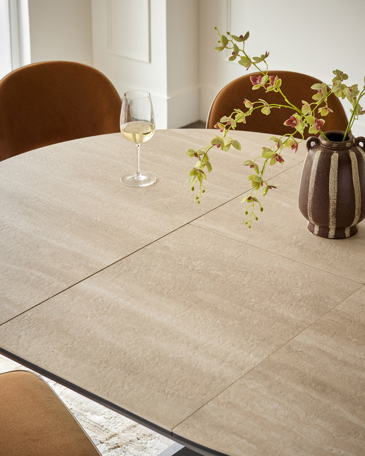 Hayden round extending dining table in natural travertine ceramic, shown extended with place setting and floral centerpiece.