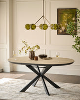 Hayden round extending dining table in natural travertine with black metal X-frame base, styled with place settings and greenery.