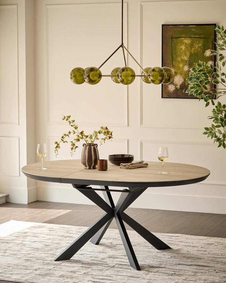 Hayden round extending dining table in natural travertine with black metal X-frame base, styled with place settings and greenery.