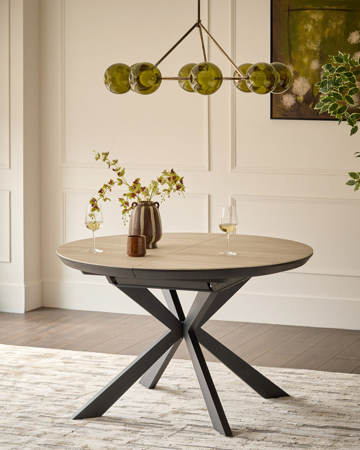 Hayden round extending dining table with natural travertine top and black metal X-frame base, styled with place settings.