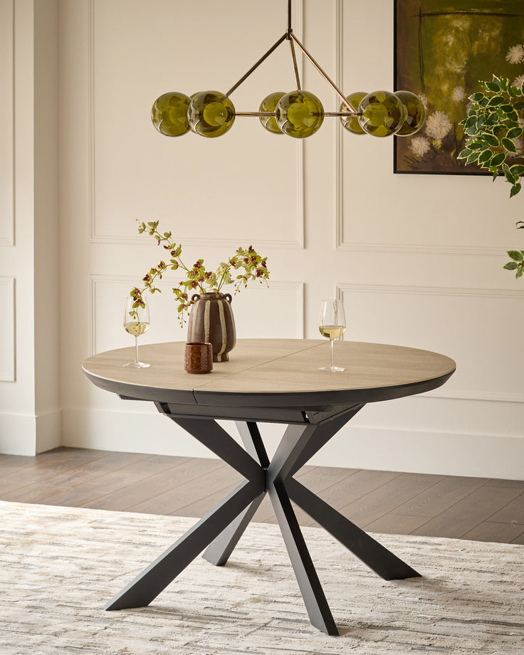 Hayden round extending dining table with natural travertine top and black metal X-frame base, styled with place settings.