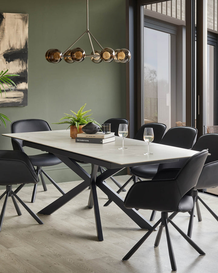 A dining room with a table, eight chairs, a light fixture and artwork against a green wall.
