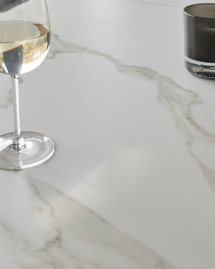 White marble dining table with elegant veining, styled with wine glasses and beverages.