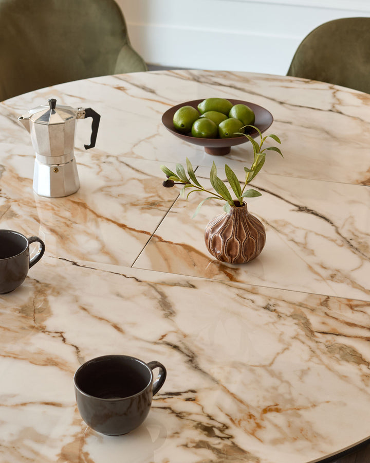 Hayden round extending dining table in natural marble finish, styled with coffee cups, olive bowl, and decorative vase.