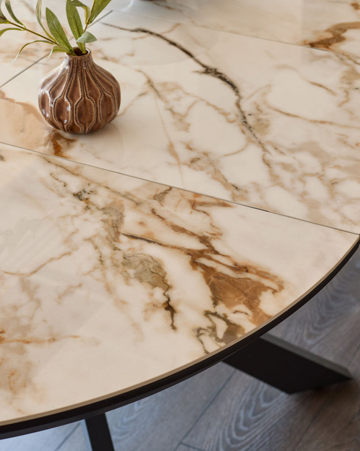 Hayden round extending dining table with natural marble top and black metal base, styled with decorative vase.