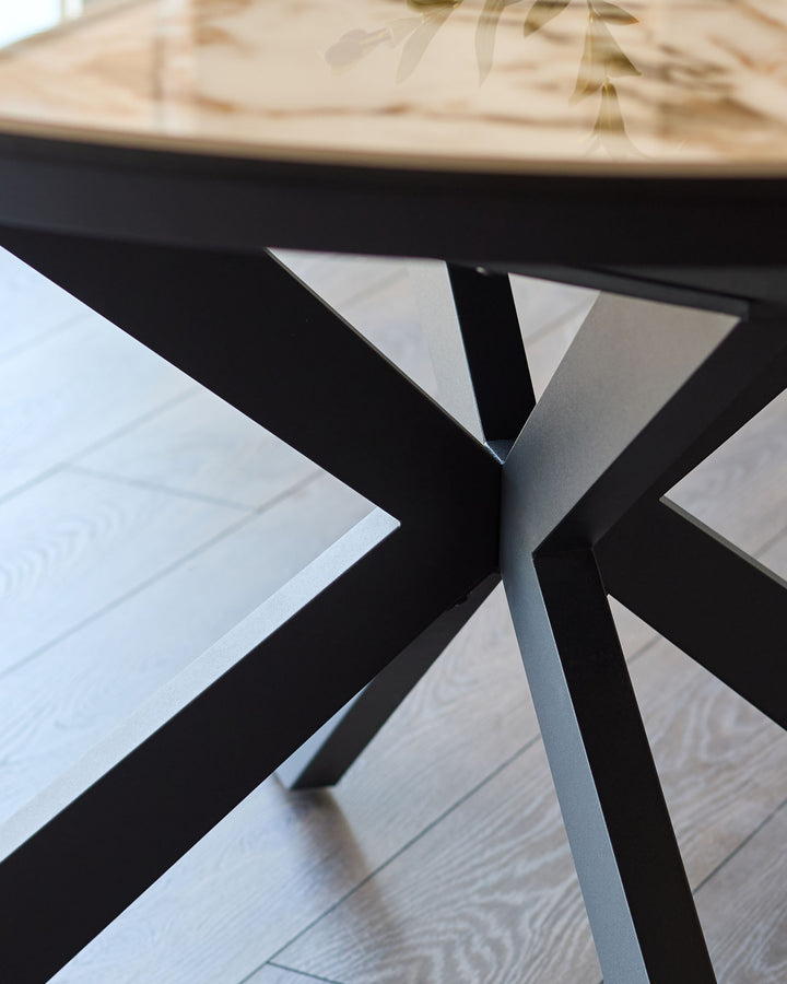 Hayden round extending dining table with black X-frame base and natural ceramic top, detail view of leg structure.