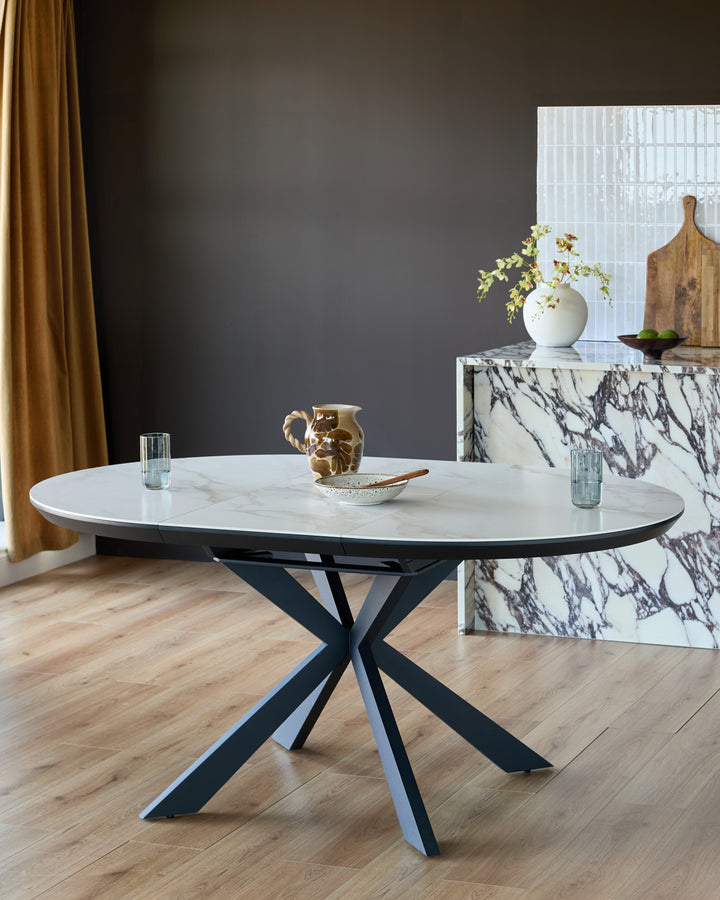 Hayden round extending dining table with white ceramic top and black X-frame base in modern interior setting.